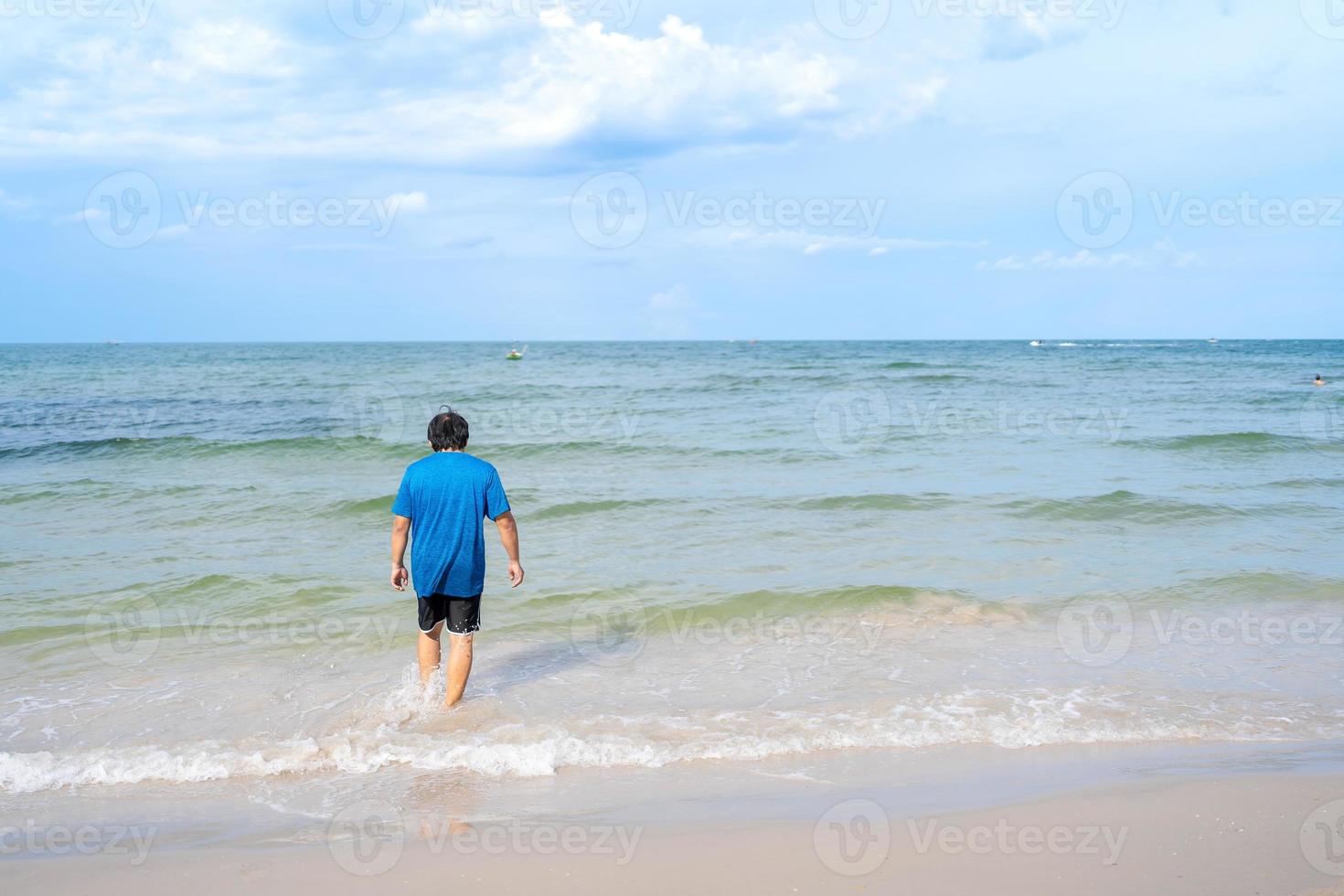 uomo asiatico nella parte posteriore che cammina nel mare dalla spiaggia, huhin, thailandia, vista sul mare con cielo blu foto