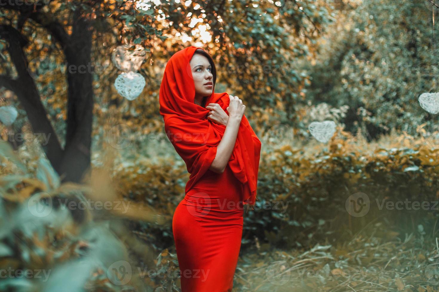bella ragazza in un vestito rosso in piedi nel giardino con i cuori foto