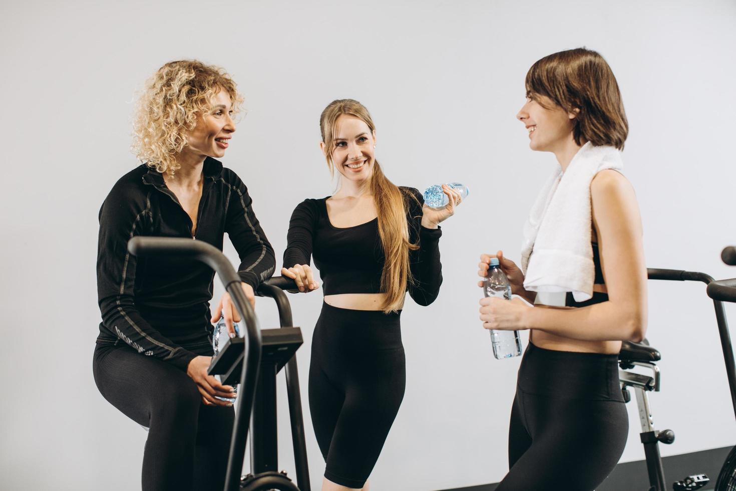 gruppo di donne in palestra che parlano tra loro di acqua potabile dopo l'allenamento in palestra sulle bici ad aria foto