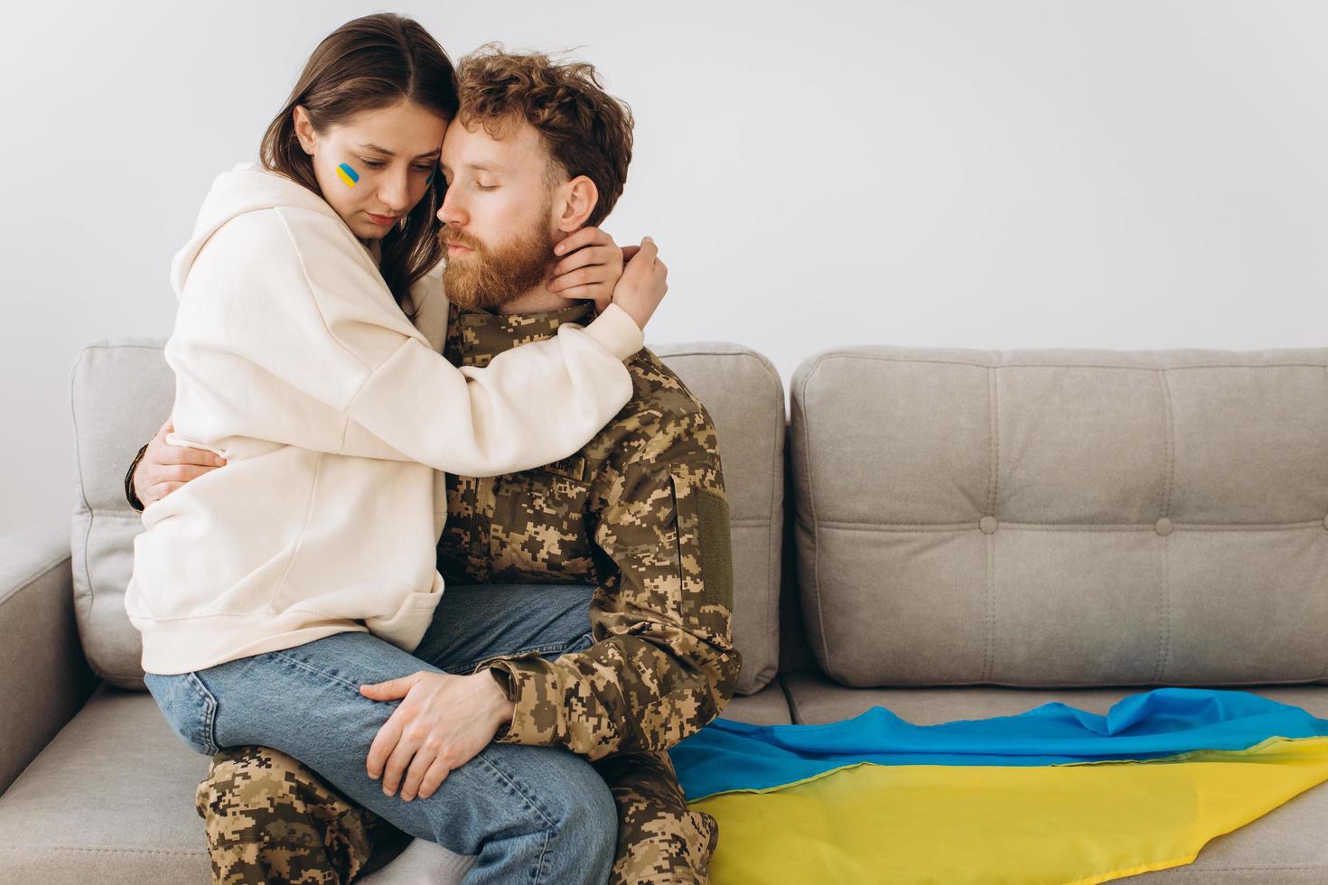 coppia ucraina, militare in uniforme con la sua ragazza sul divano di casa su uno sfondo di bandiera gialla e blu foto