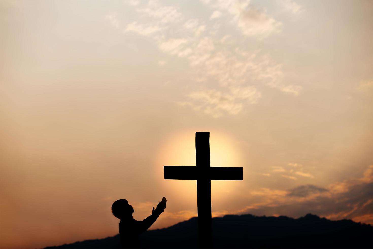 sagoma di una preghiera uomo davanti alla croce sulla montagna al tramonto. concetto di religione. foto