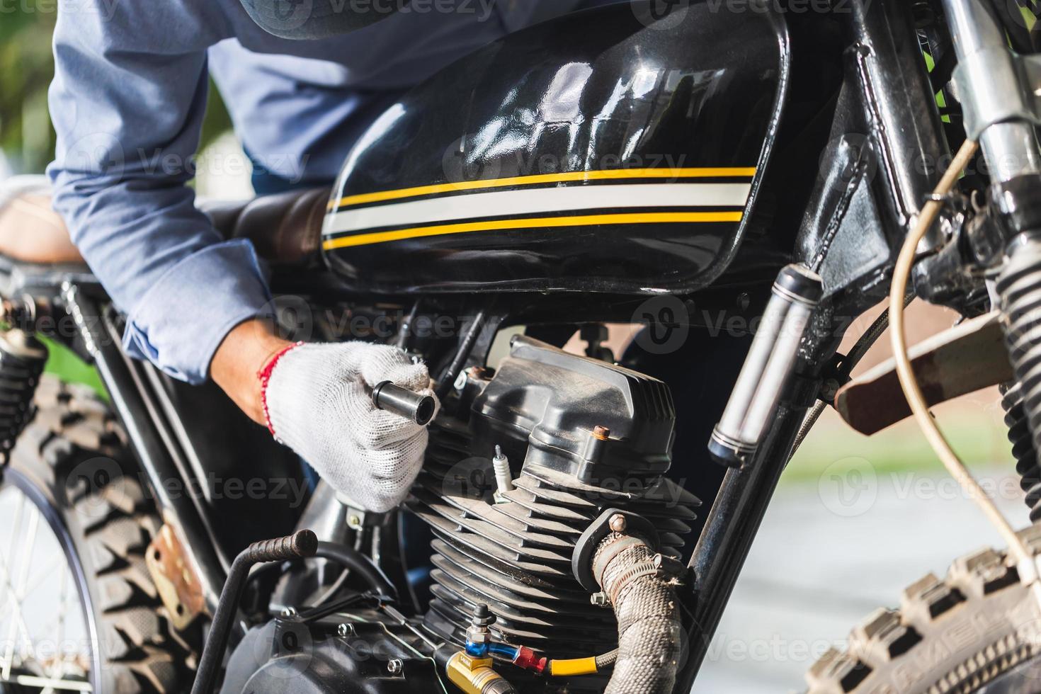 controllo meccanico della candela del motociclo nel garage dell'officina, uomo che ripara la moto in officina, concetti di riparazione e manutenzione foto