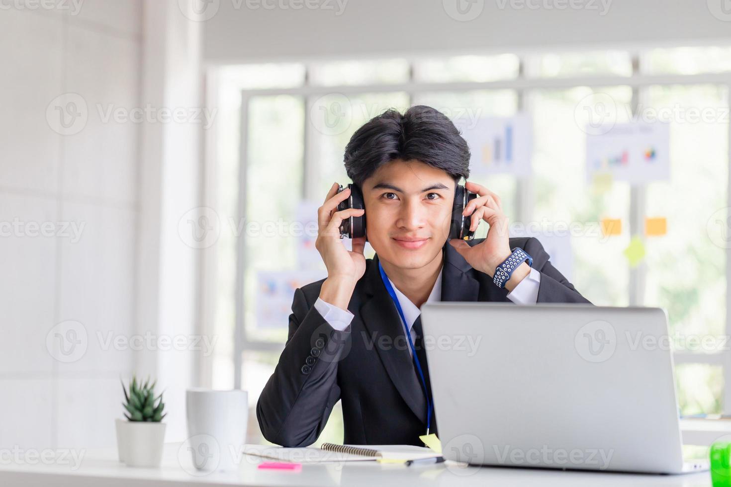 allegro giovane uomo d'affari ascolta la traccia audio tramite cuffie stereo, sorridente uomo in auricolari che lavora in ufficio foto