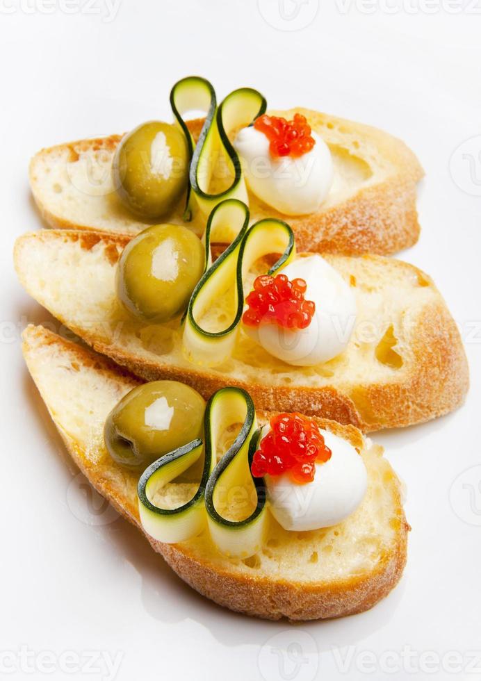 bruschetta con mozzarella, olive verdi, zucchine e caviale rosso foto