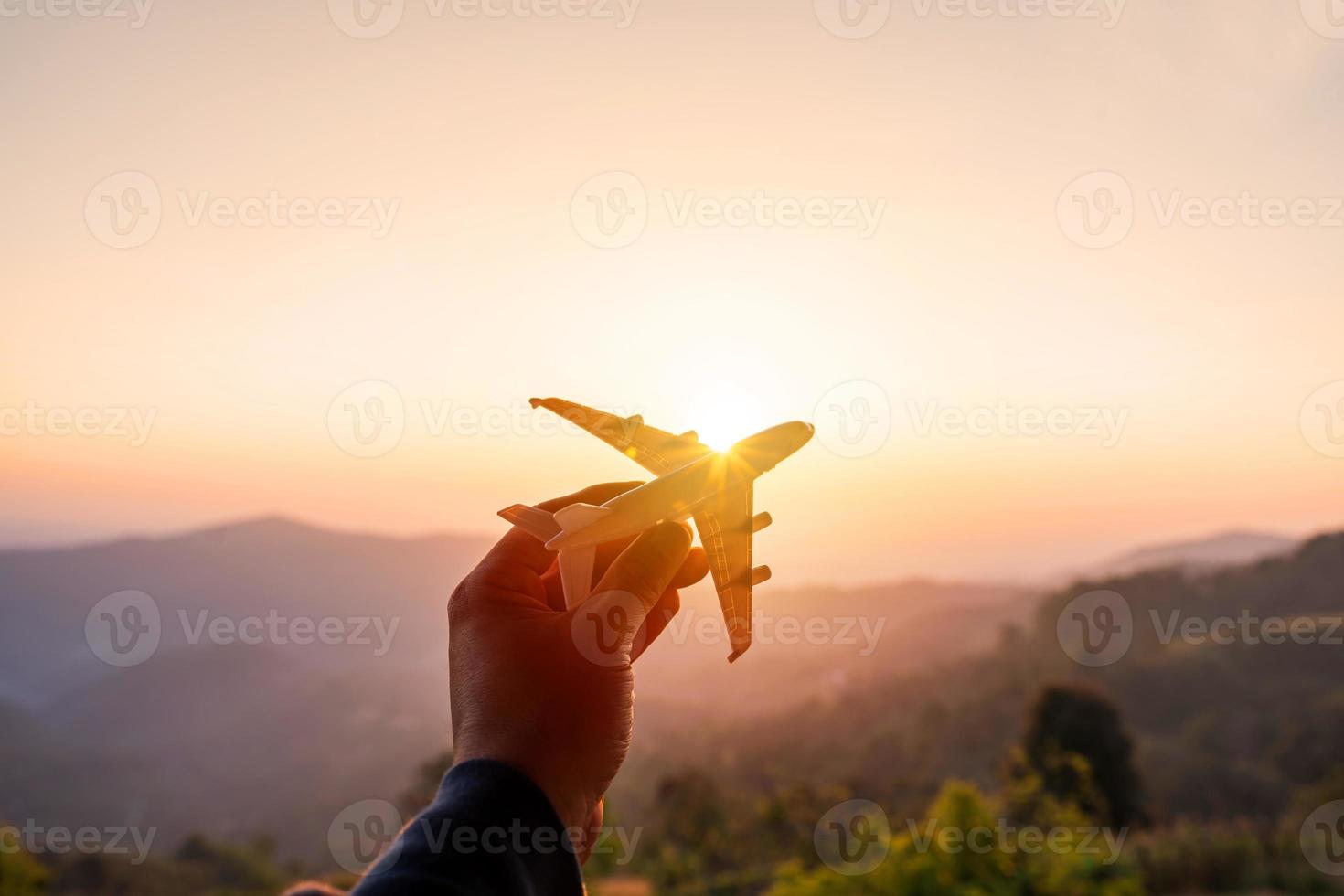 mano che tiene un aeroplano in miniatura con vista sulle montagne all'alba, vacanze estive e concetto di viaggio foto