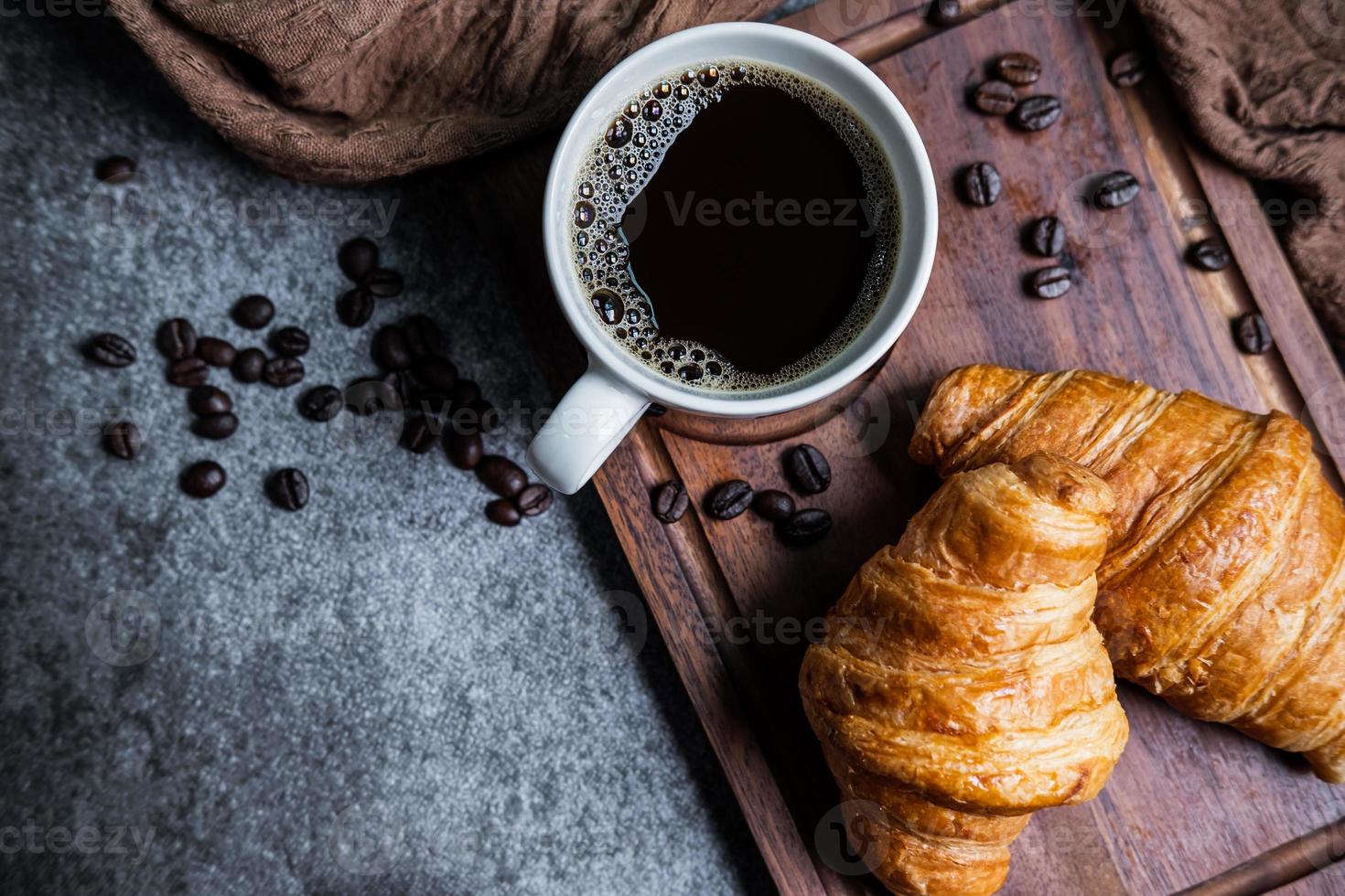 colazione con croissant freschi e tazza di caffè nero su tavola di legno foto