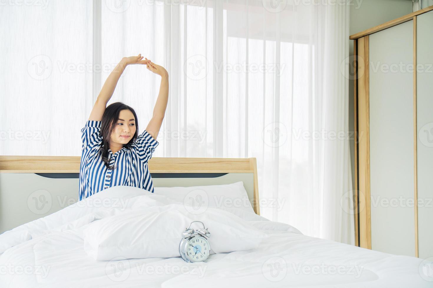 bella giovane donna che si allunga a letto con le braccia alzate dopo il risveglio, stile di vita sano, concetto di benessere foto