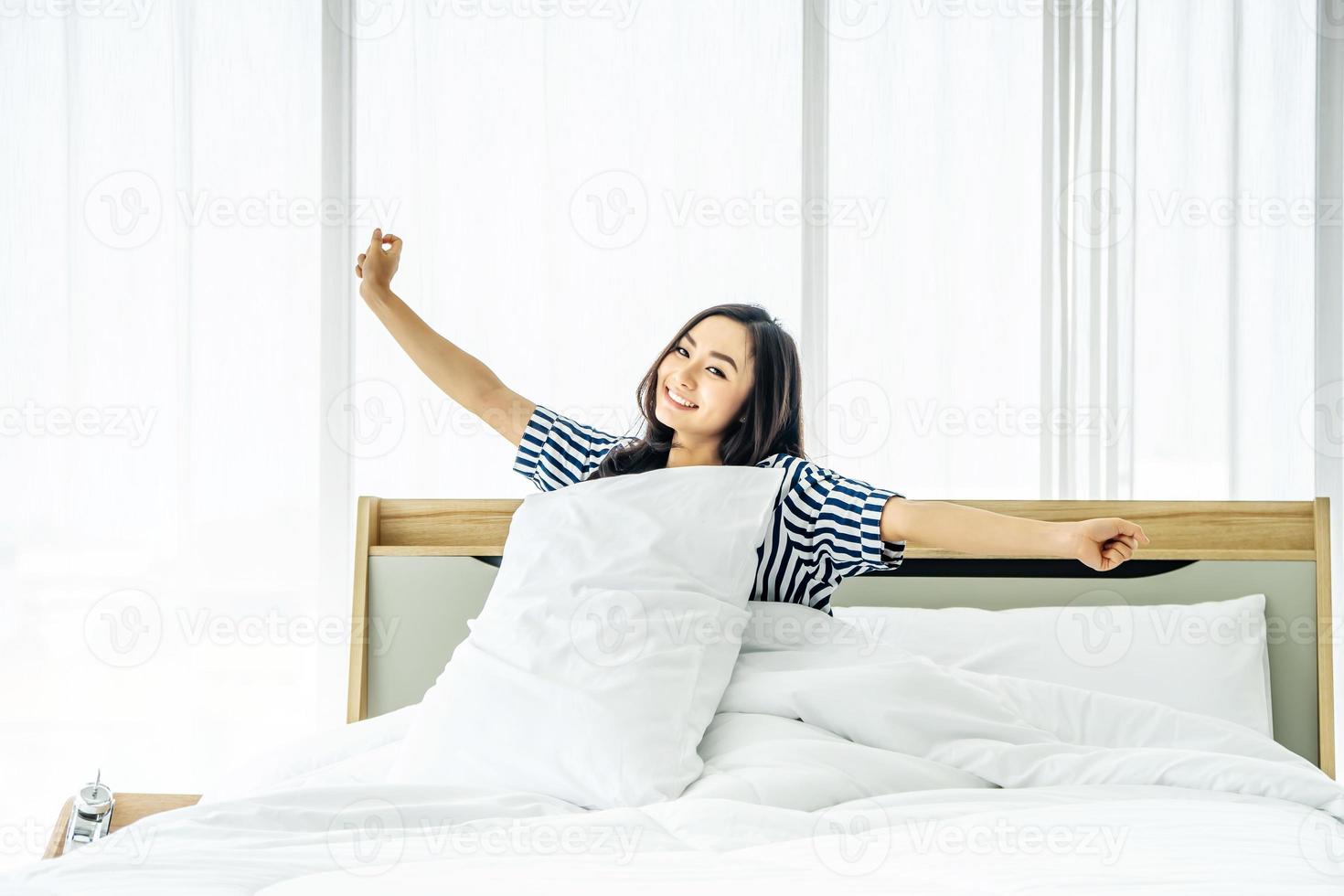 bella giovane donna che si allunga a letto con le braccia alzate dopo il risveglio, stile di vita sano, concetto di benessere foto
