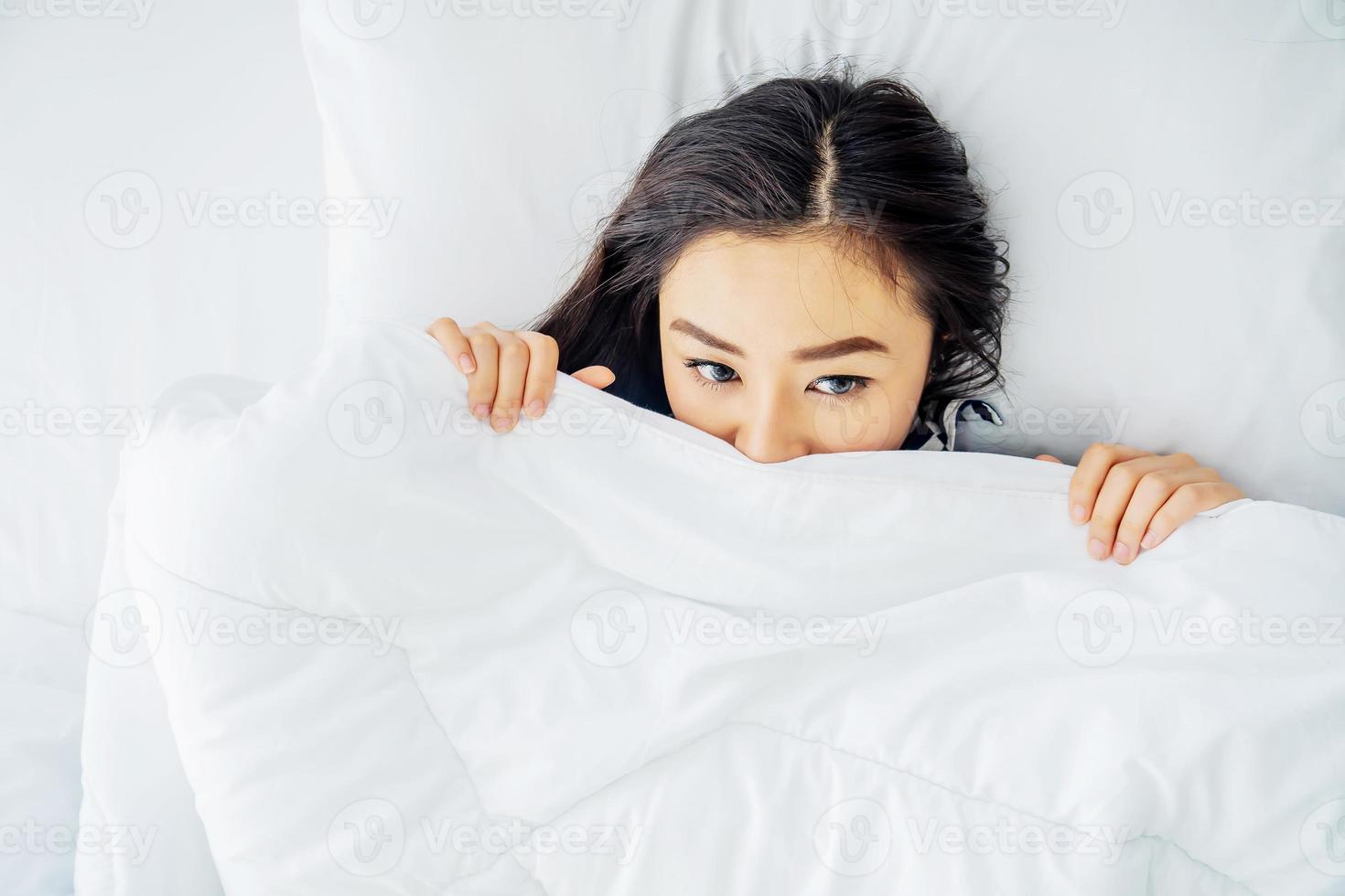 svegliati. bella giovane donna asiatica solitaria che si sveglia dopo una buona notte di sonno, la mattina a letto coprendosi il viso sotto la coperta, vista dall'alto, copia spazio. foto