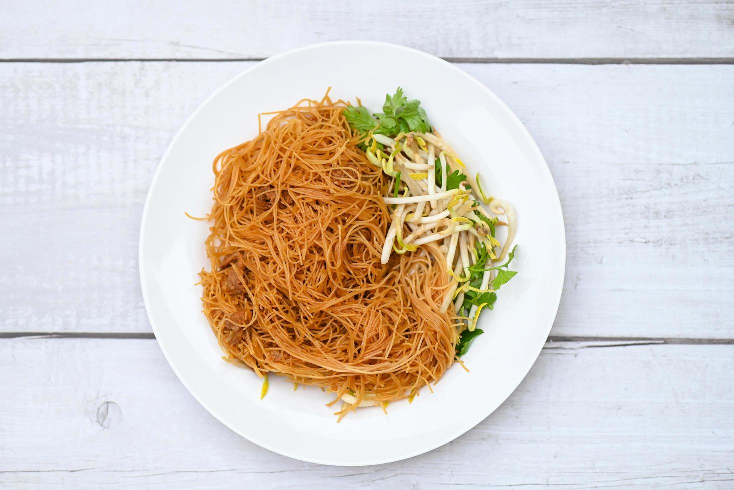 Vermicelli di noodles fritti su piatto bianco, noodle fritti in stile cinese con germogli di soia e coriandolo su tavola di legno - cibo tailandese foto