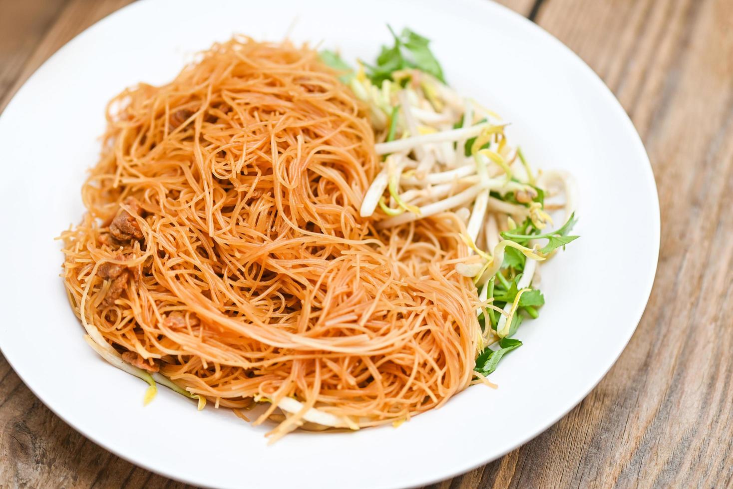 Vermicelli di noodles fritti su piatto bianco, noodle fritti in stile cinese con germogli di soia e coriandolo su tavola di legno - cibo tailandese foto