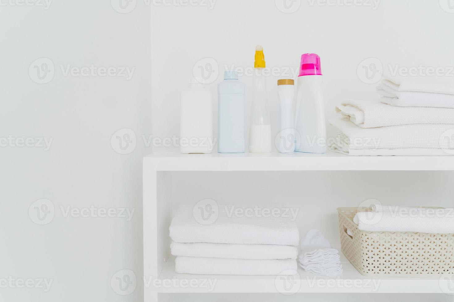pila di asciugamani bianchi puliti con detersivi sulla console isolata su sfondo bianco. biancheria fresca e detersivo liquido in bagno foto