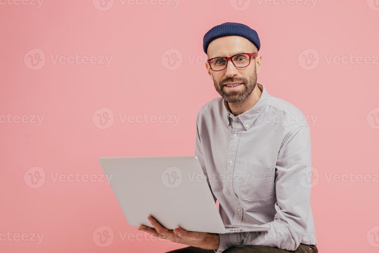 il blogger maschio con la barba lunga aggiorna il suo profilo, naviga sui social network, condivide file multimediali con i follower, è connesso a Internet senza fili, tiene in mano un computer portatile, indossa abiti eleganti e formali foto