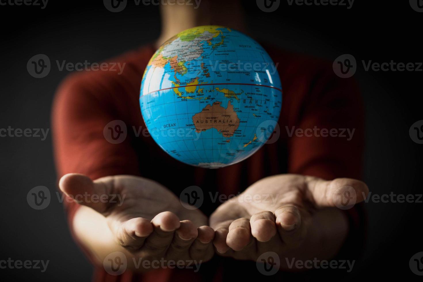 primo piano di un globo che galleggia sopra la mano di un uomo su uno sfondo sfocato. concetto di giorno della terra con foto a tono basso