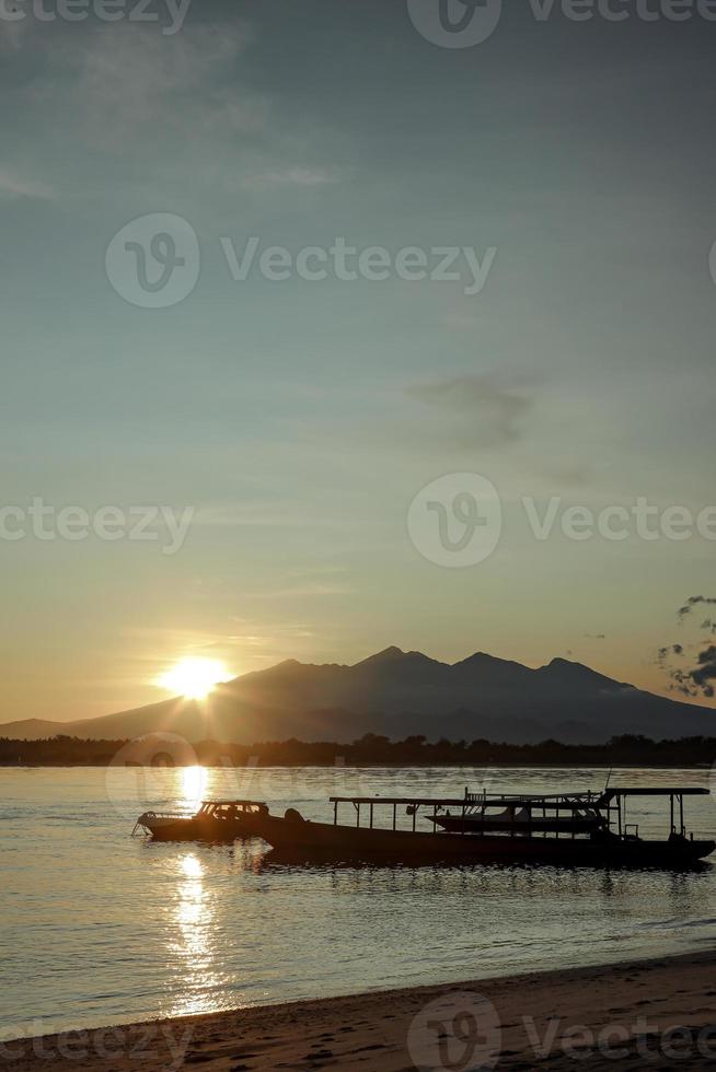 alba dietro la montagna con barche da pesca a coda lunga barche tradizionali sul mare a gili trawangan, bali, indonesia foto