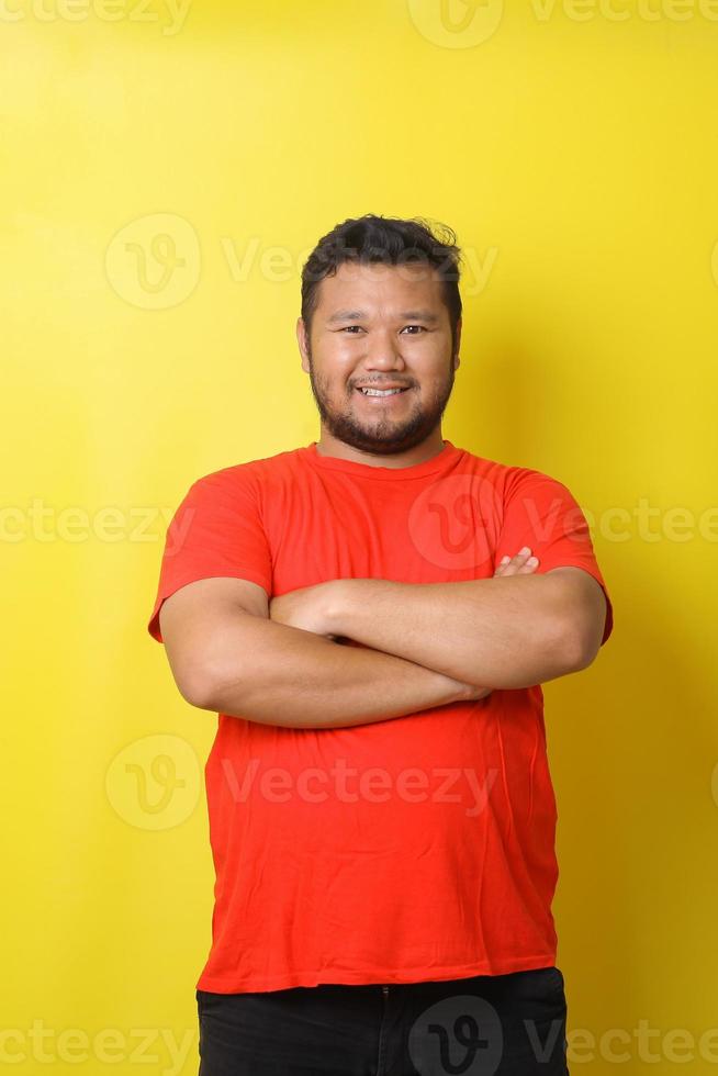 uomo asiatico grasso felice che sorride mentre piega le braccia isolate su sfondo giallo foto