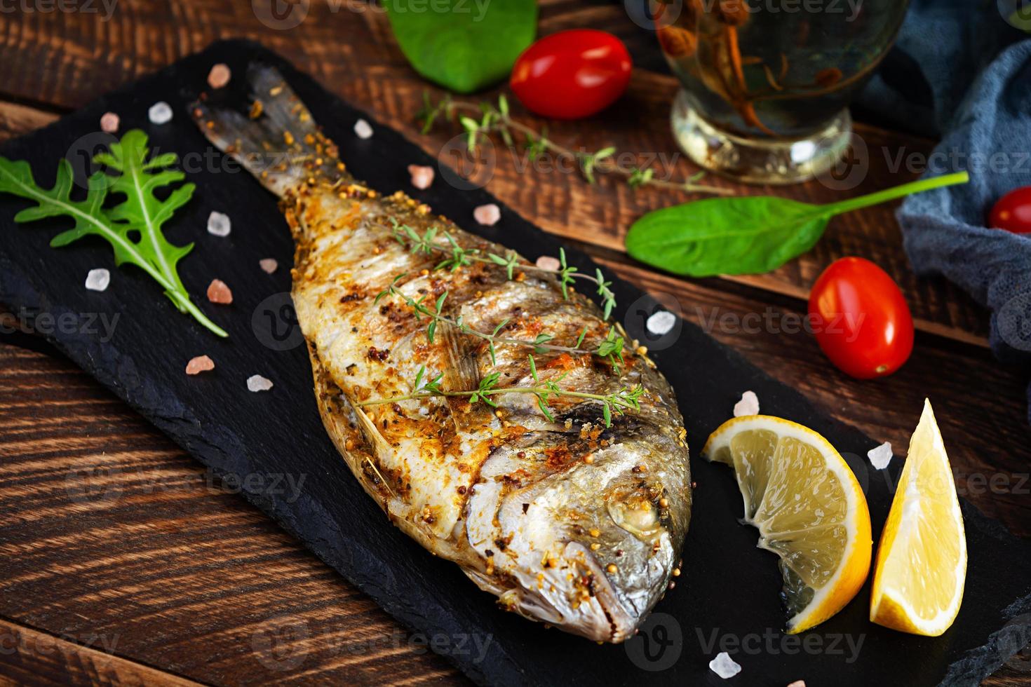 pesce dorado alla griglia su fondo di legno. pesce di mare arrosto con spezie ed erbe aromatiche foto