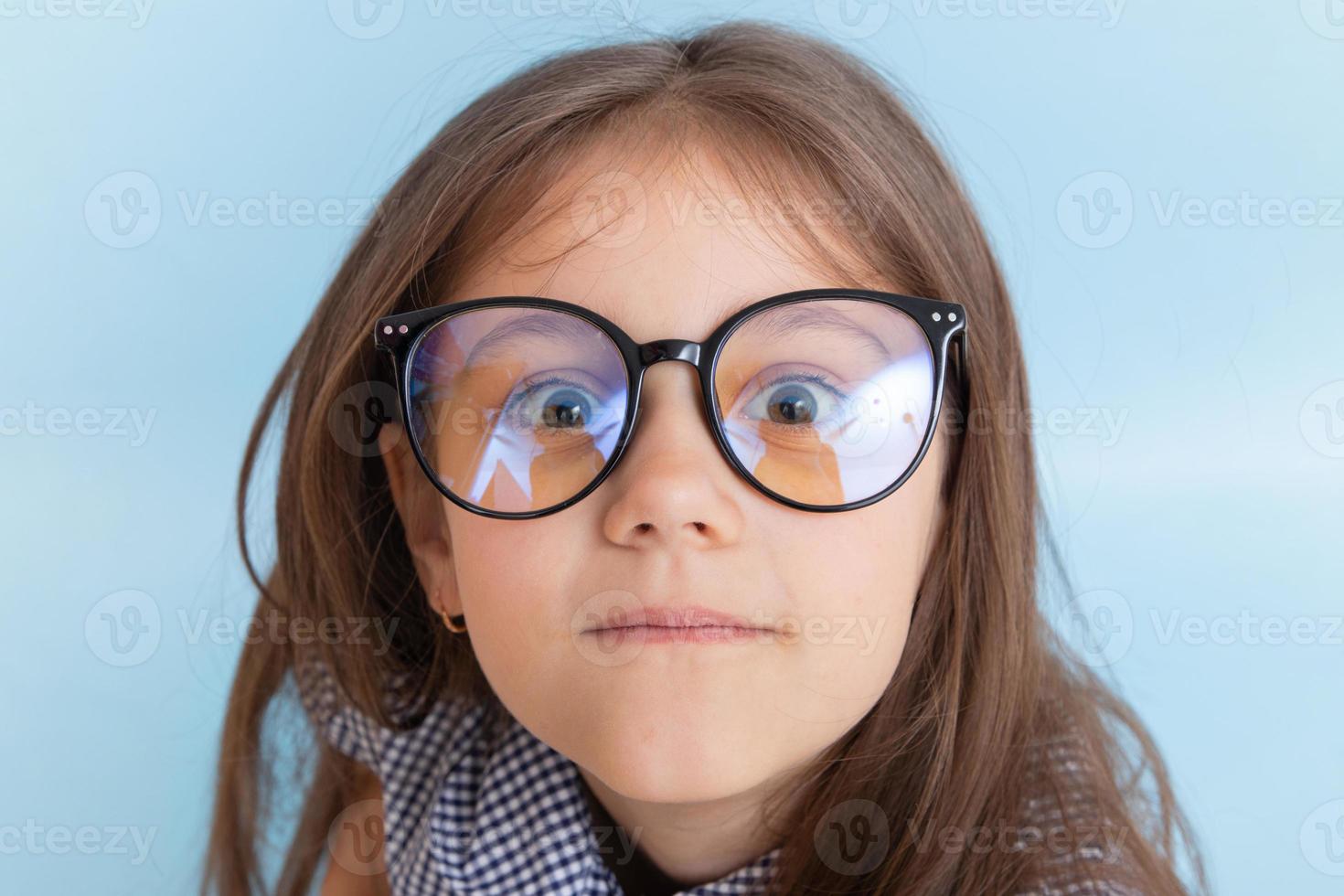 il ritratto di una bambina di 7 anni con i capelli lunghi in occhiali con occhi sporgenti guarda la telecamera foto