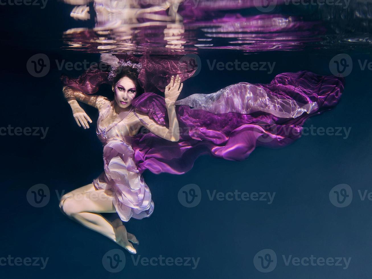 donna in abiti colorati sullo sfondo scuro che nuota sott'acqua foto