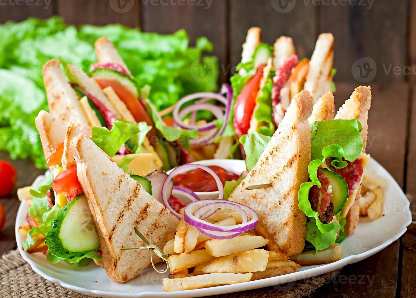 club sandwich con formaggio, cetriolo, pomodoro, carne affumicata e salame. servito con patatine fritte. foto