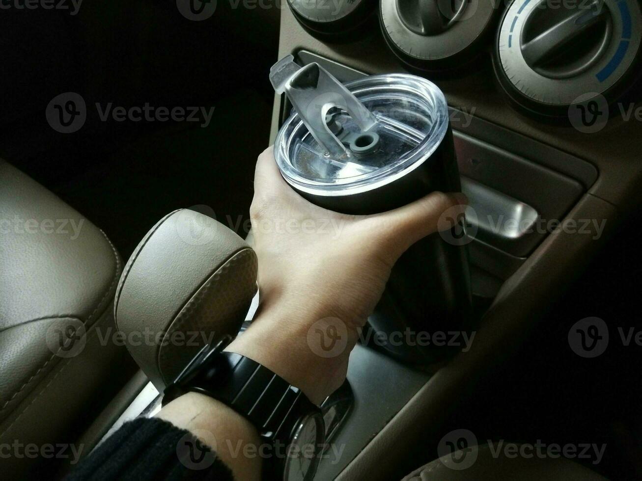 la mano di una donna sta raccogliendo una tazza termica in acciaio inossidabile nera posta nell'auto. foto