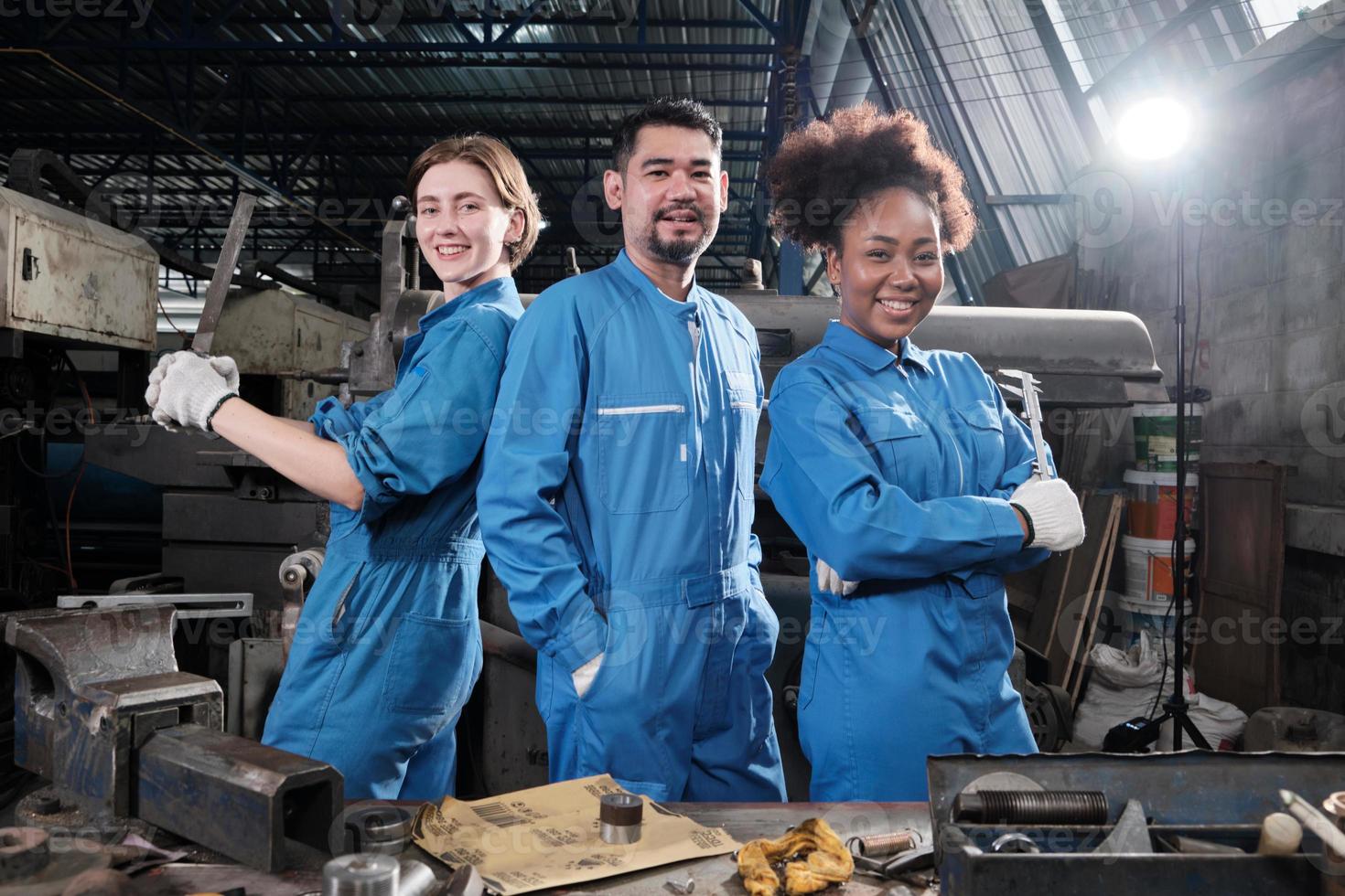 i lavoratori dell'industria multirazziale in uniforme di sicurezza collaborano con l'unità, agiscono con gli strumenti ed esprimono un lavoro felice insieme con un sorriso e allegro in una fabbrica meccanica, occupazione di ingegnere professionista. foto