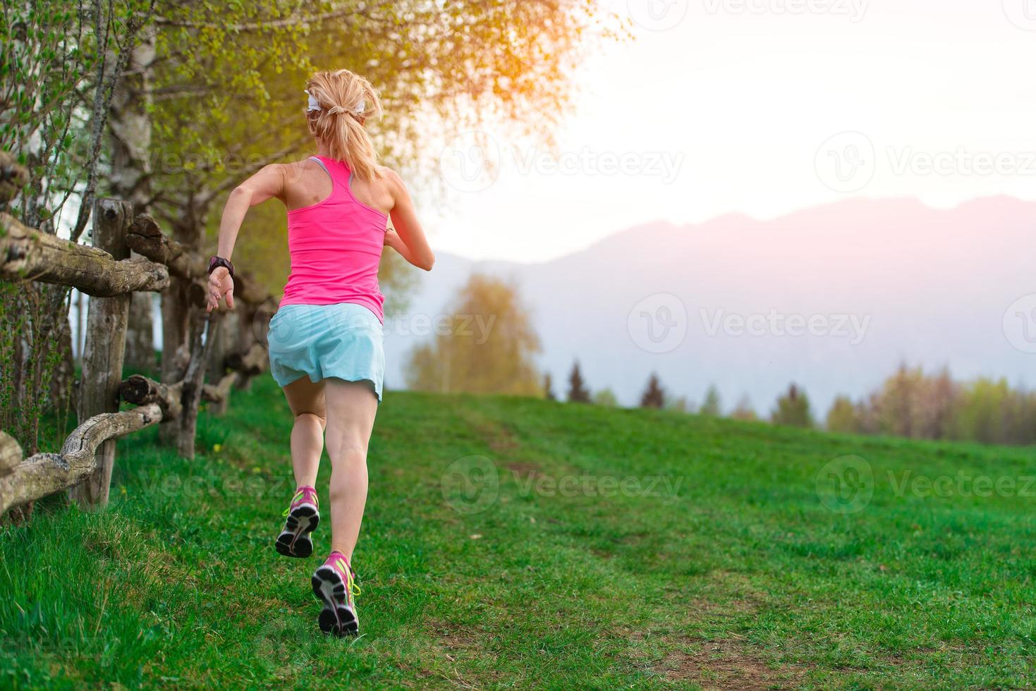 atleta ragazza bionda corre un sentiero di montagna nell'erba verde foto