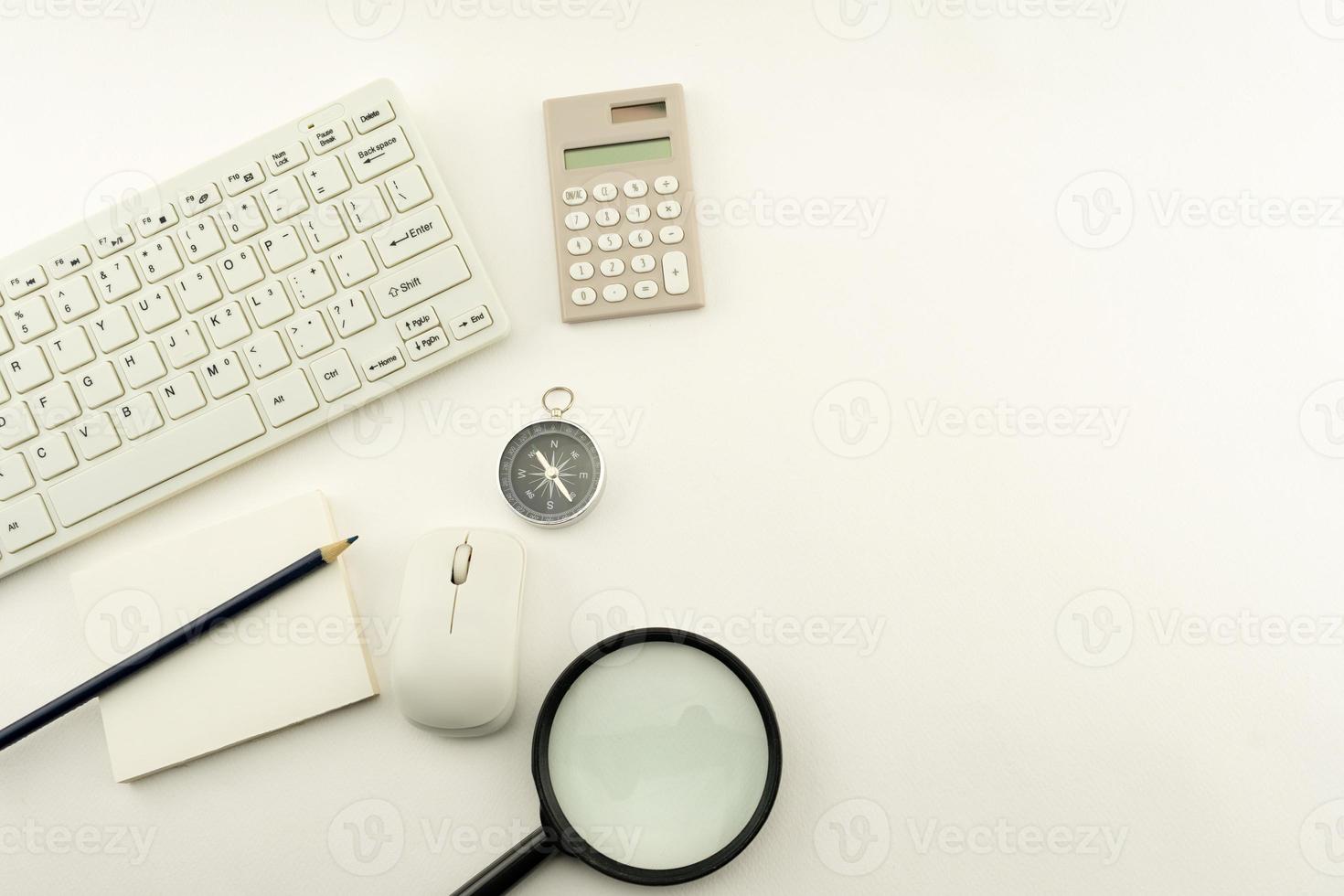 oggetti aziendali di pc, tastiera, mouse, matita, bussola e calcolatrice, lente d'ingrandimento su sfondo bianco tavolo. foto