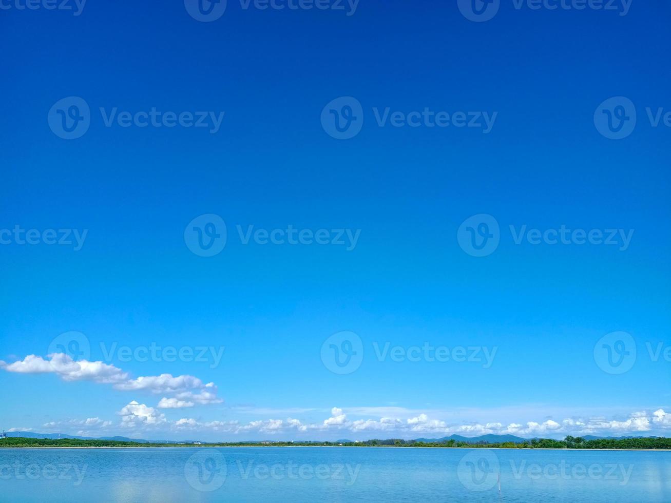 riflesso del cielo blu e della nuvola bianca sulla superficie del lago con la linea dell'albero e la piccola montagna foto