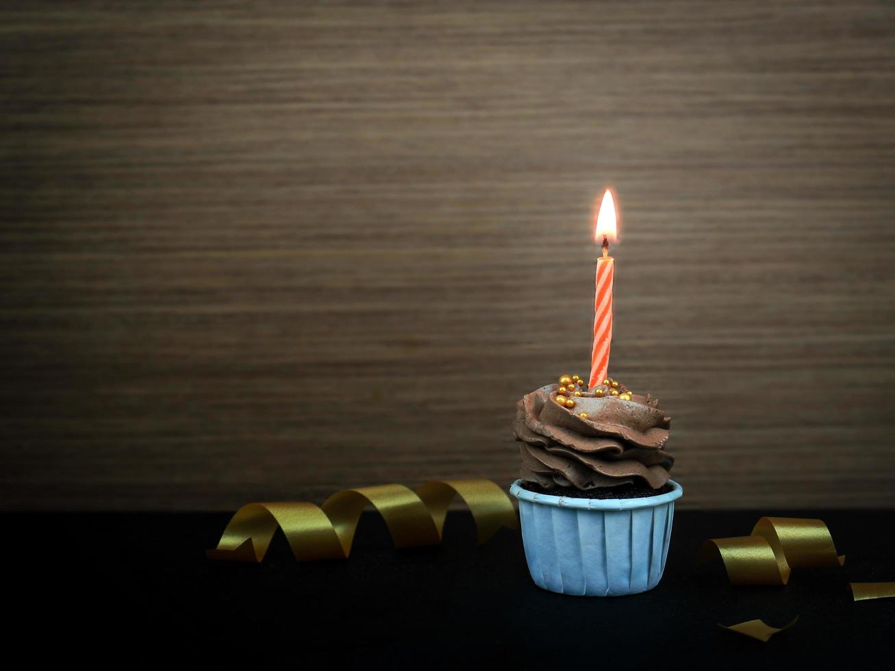 Cupcake al cioccolato al caffè dolce con candela di prua su sfondo di legno con spazio per la copia. concetto di sfondo festa di buon compleanno. foto