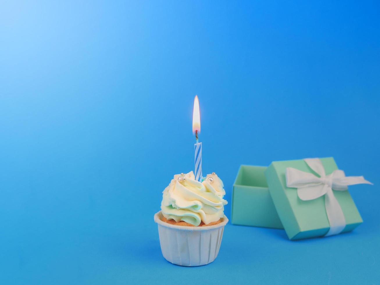 Cupcake dolce con candela di prua e confezione regalo su sfondo blu con spazio per la copia. concetto di sfondo festa di buon compleanno. foto