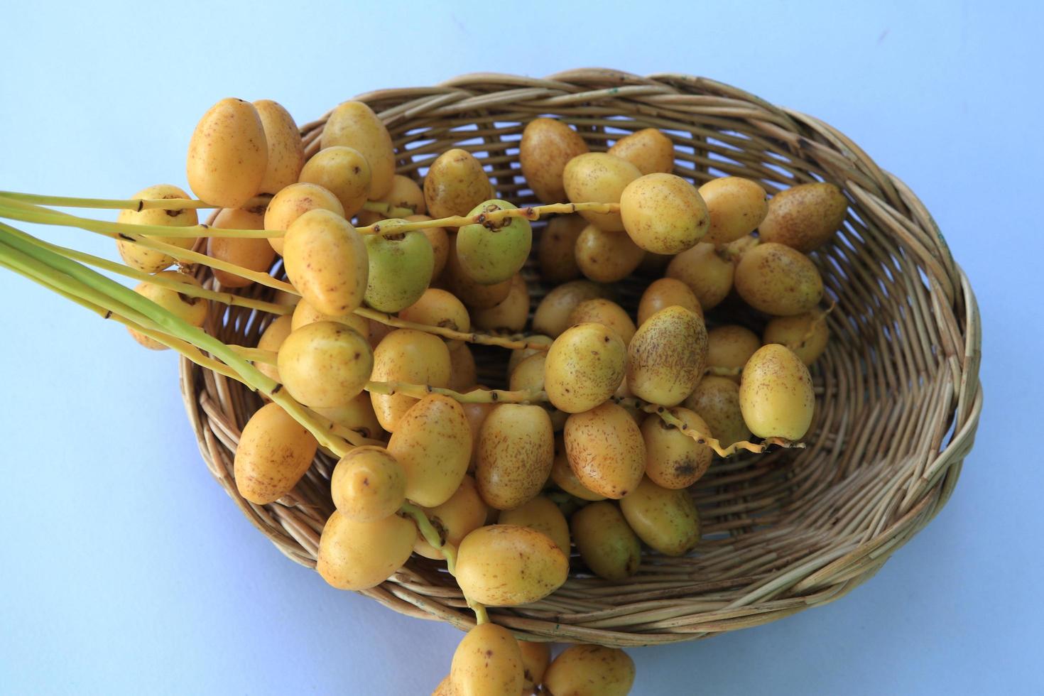 i datteri gialli maturi sono coltivati biologicamente, dolci e deliziosi e freschi in un cesto intrecciato su sfondo blu e bianco con le mani di un uomo che li tiene. foto