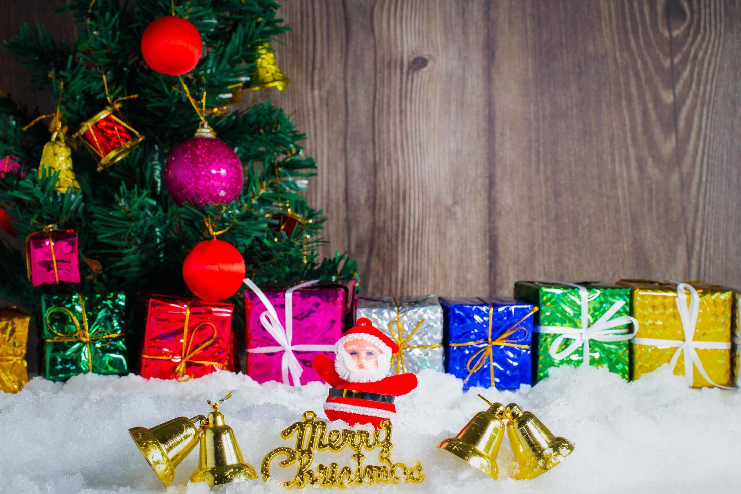 bambola di babbo natale e decorazioni poste sulla neve e sullo sfondo dell'albero di natale e fuoco selettivo in legno foto