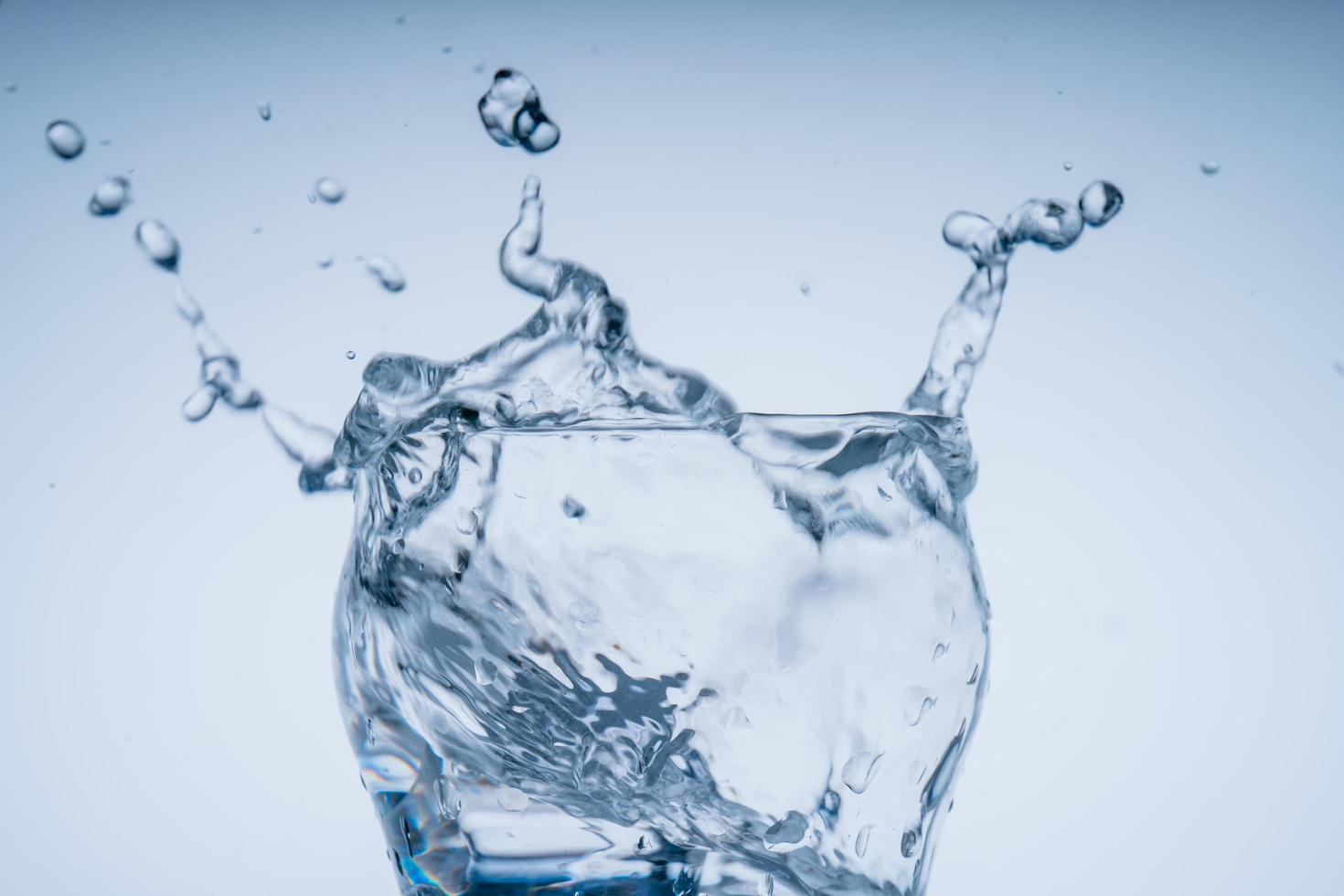 il cubetto di ghiaccio è caduto nel bicchiere d'acqua. acqua schizzata dal vetro trasparente. concetto fresco foto