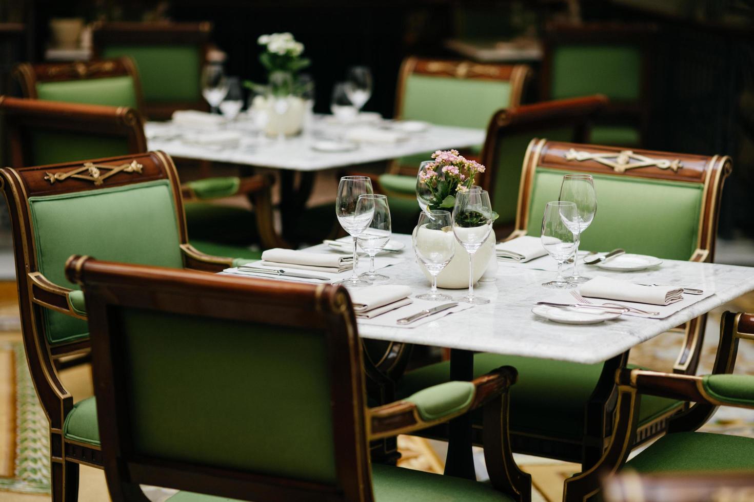 tavola servita con bicchieri di lusso, posate, fiori, sedie verdi intorno nell'accogliente ristorante. nessuno in tiro. tavola decorata per evento festivo foto