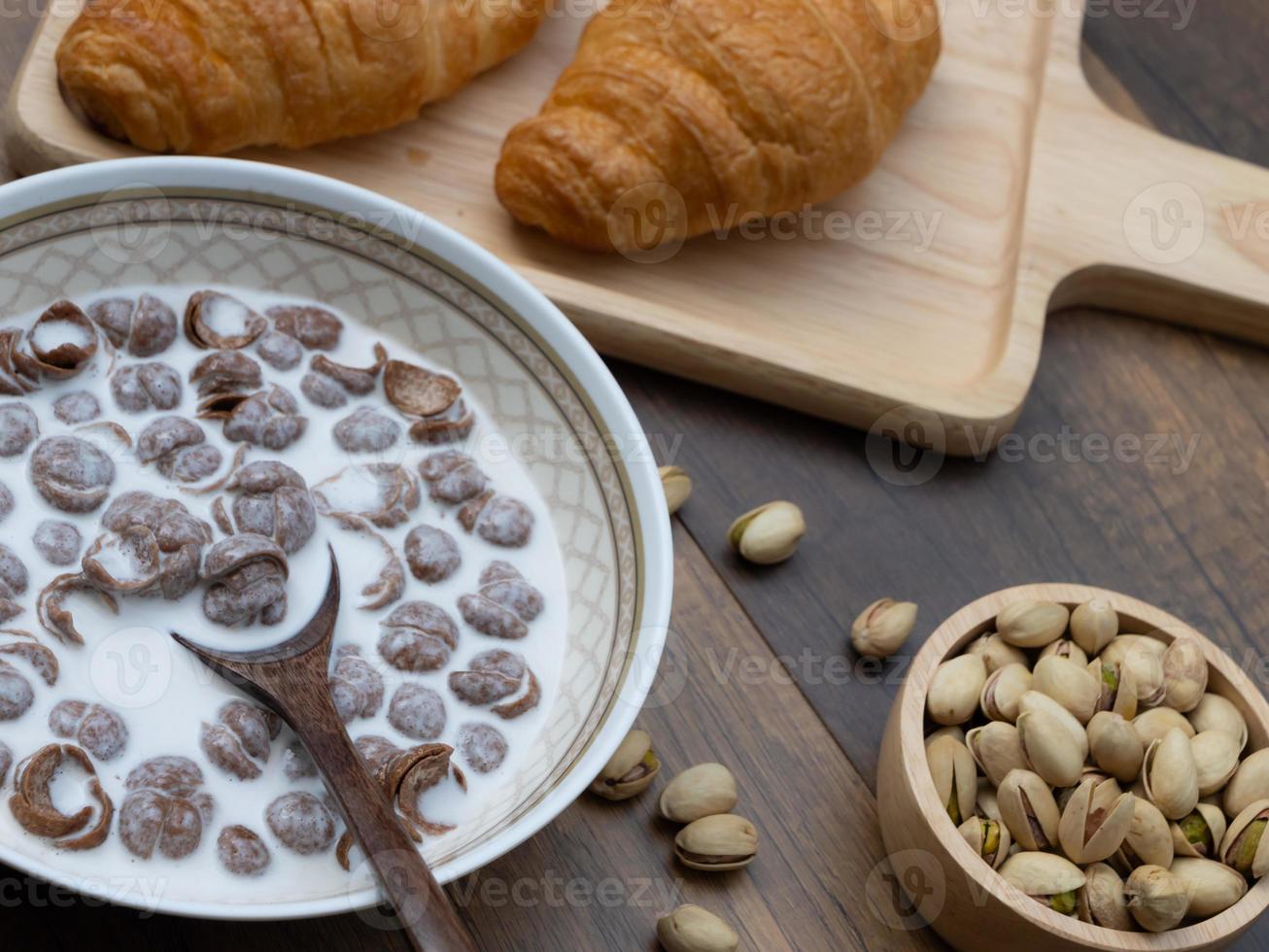 primo piano di cereali per la colazione con latte, croissant e pistacchi su fondo di legno. foto
