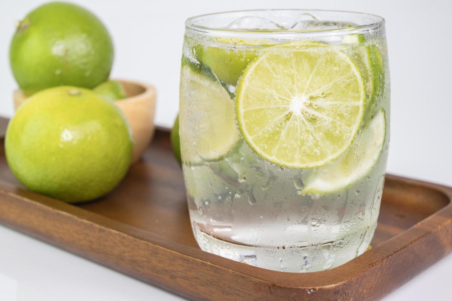 bevanda fredda dal limone tagliato a pezzi in bicchiere d'acqua su tazza di legno foto