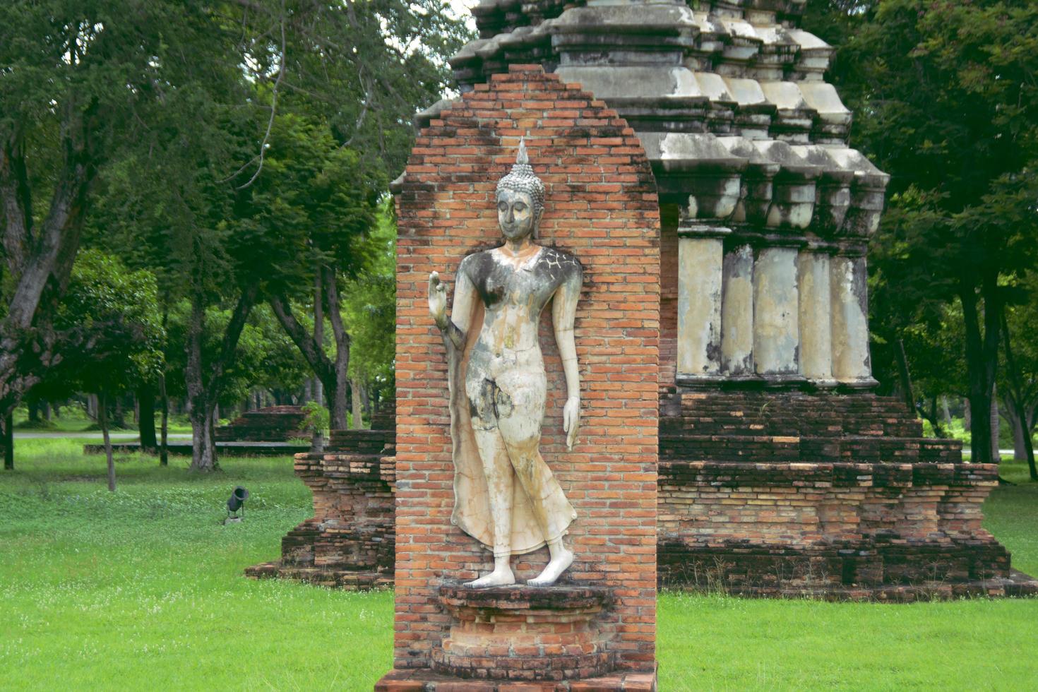 la statua del buddha ambulante davanti al vecchio muro di mattoni nel parco storico di sukhothai. foto