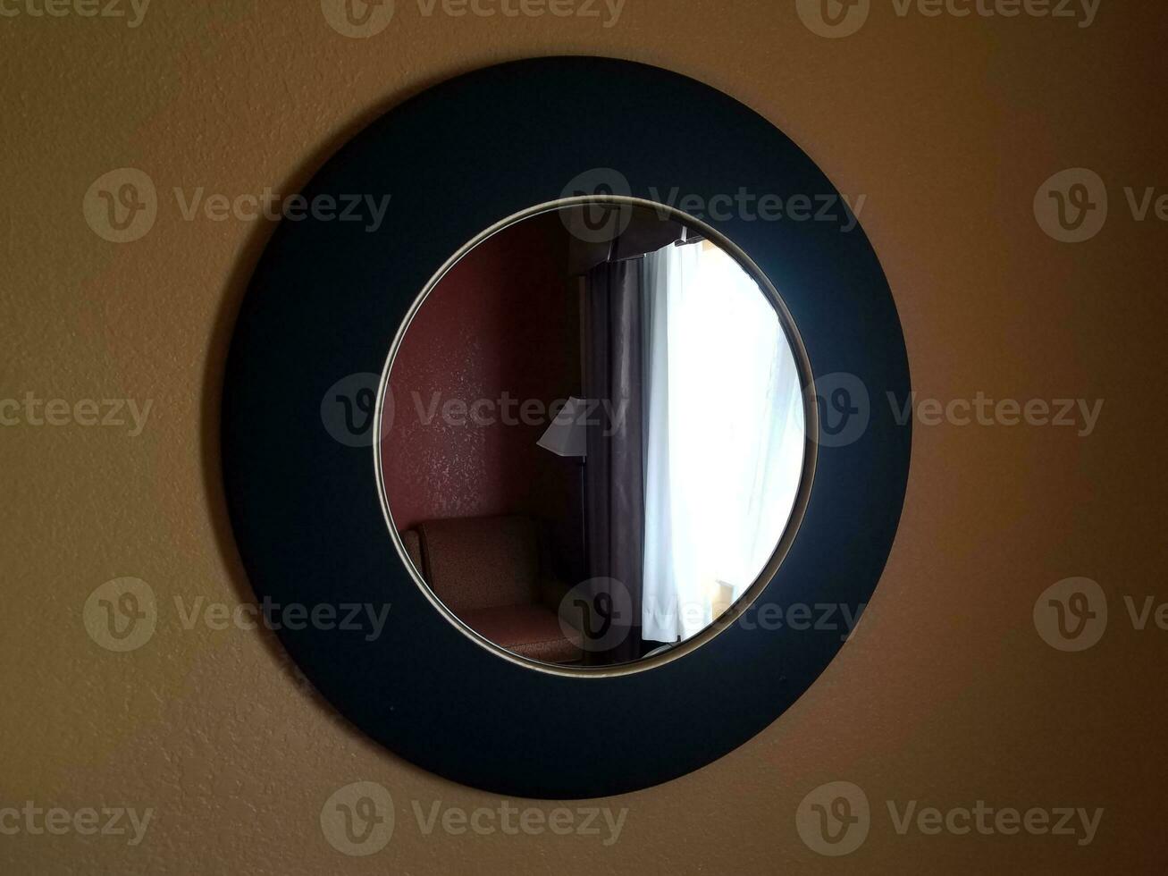 Specchio circolare nero dell'hotel sulla parete con finestra e sedia foto