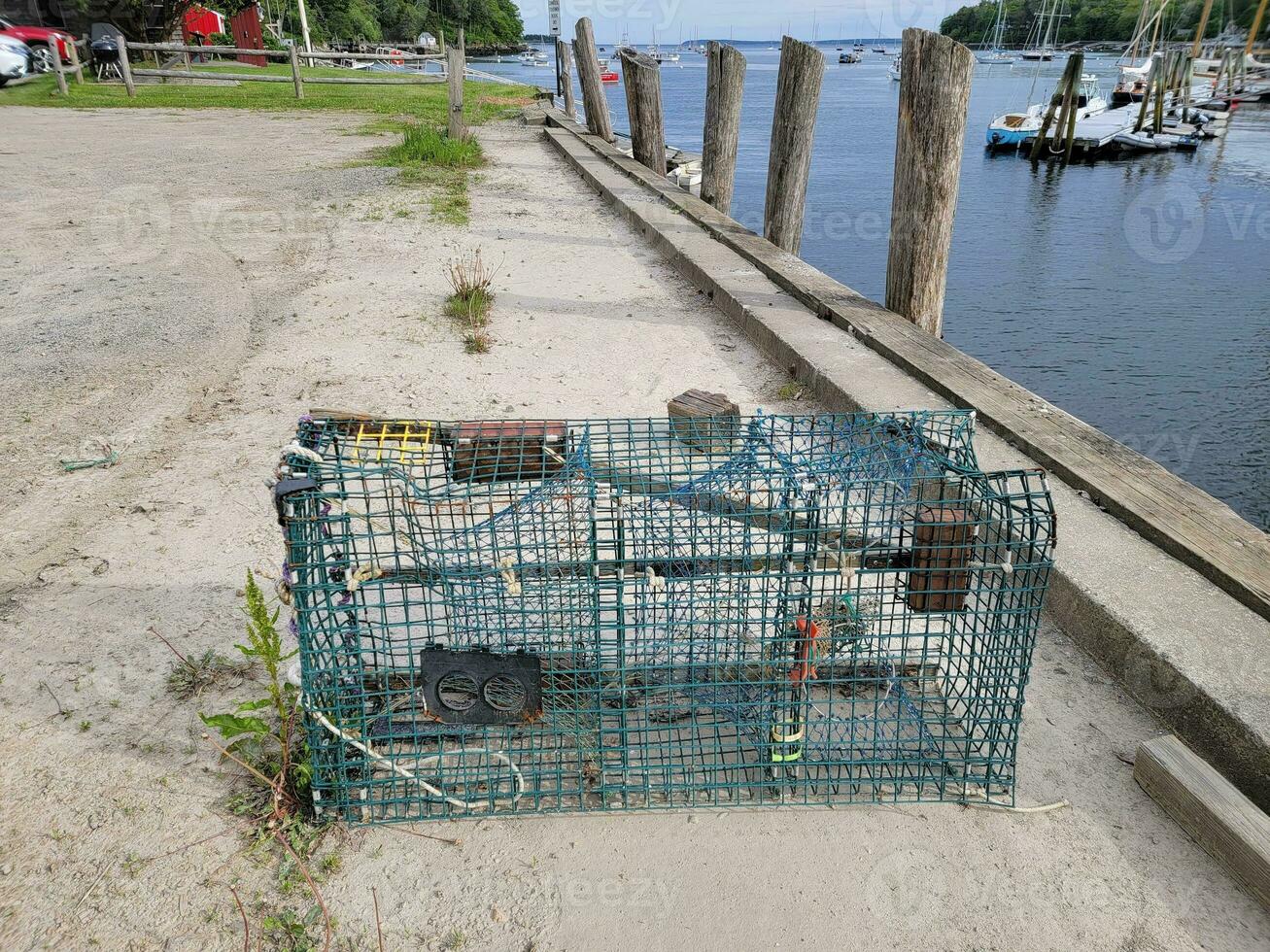 trappola per aragoste o gabbia sul molo con acqua e barche foto