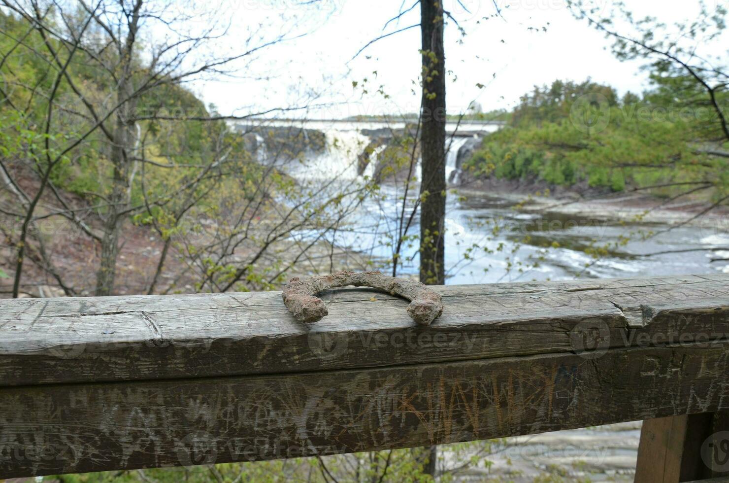 ferro di cavallo arrugginito sulla ringhiera di legno marrone con cascata sullo sfondo foto