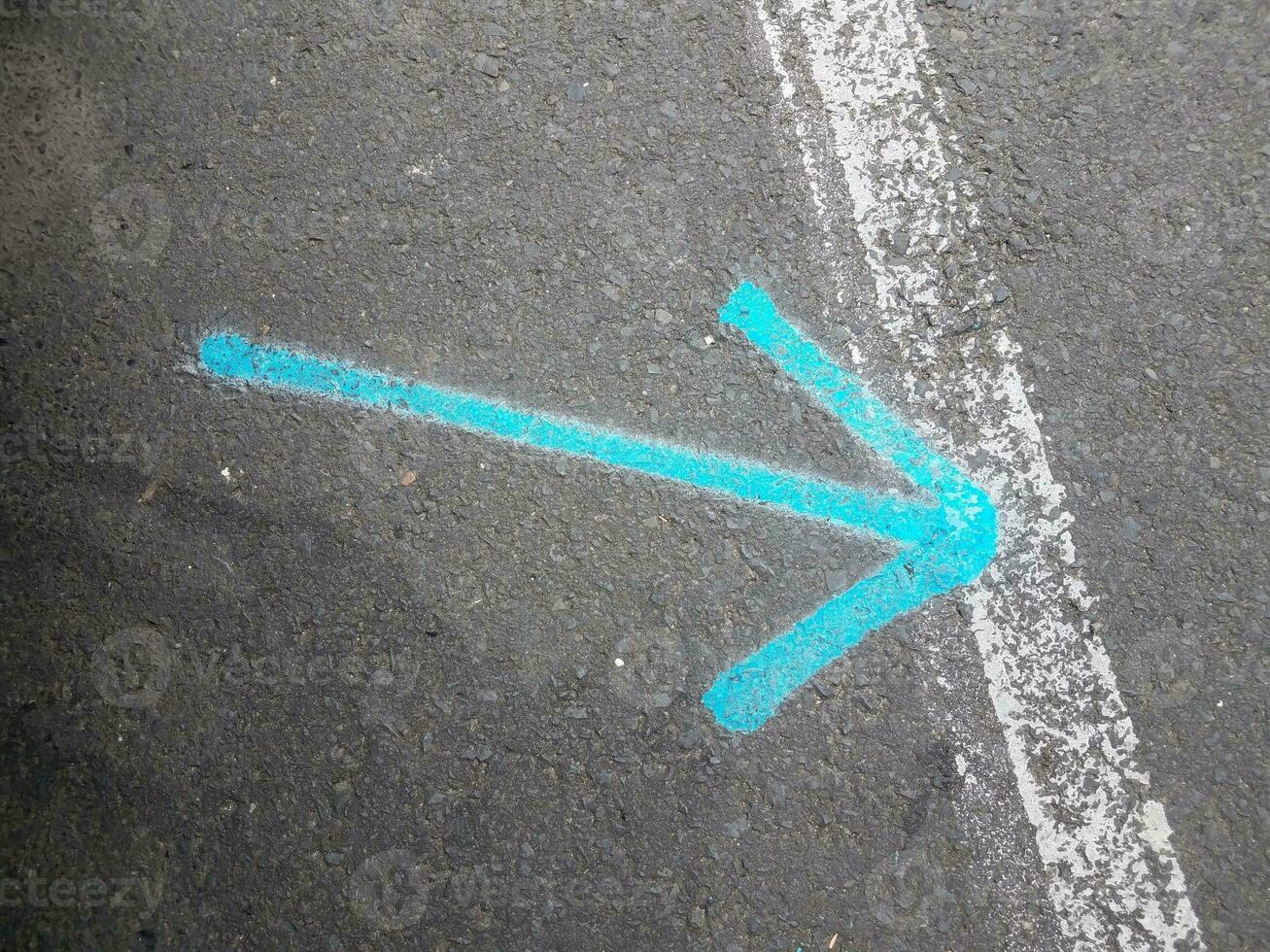 freccia blu o puntatore su asfalto nero con linea bianca foto