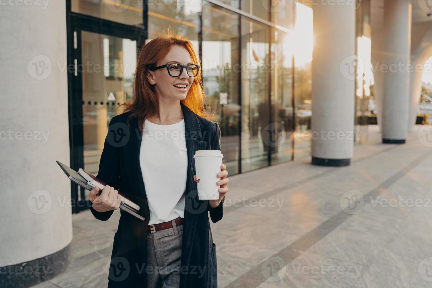 il modello femminile tiene il taccuino del touchpad e la tazza di caffè da asporto pone all'aperto durante la giornata di sole foto