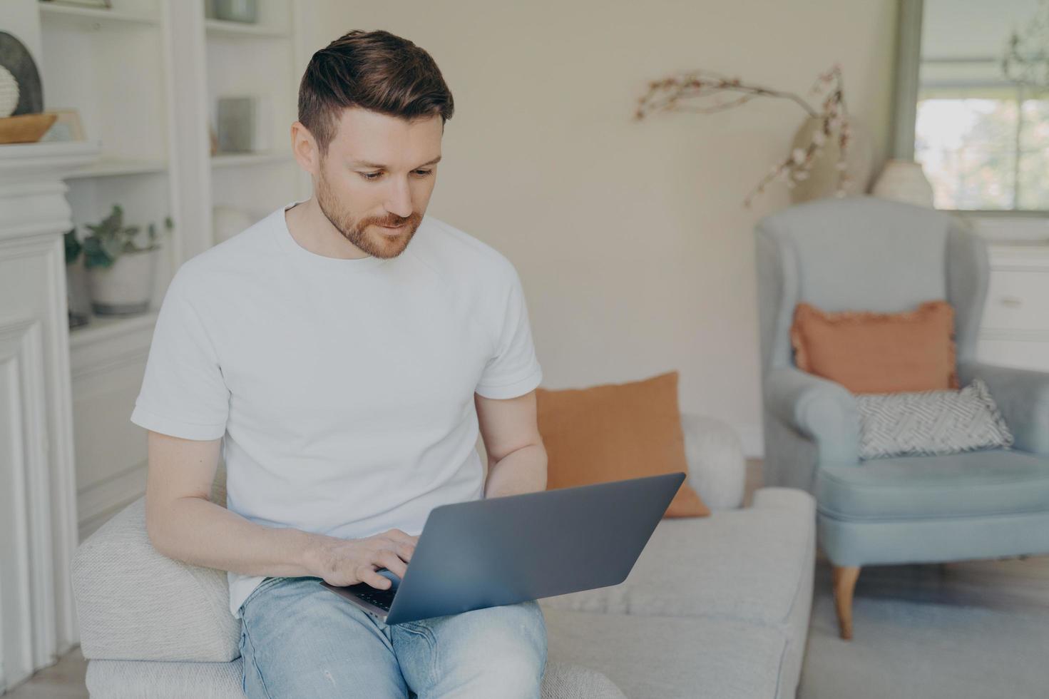 giovane serio che utilizza un computer portatile per il lavoro a distanza da casa foto