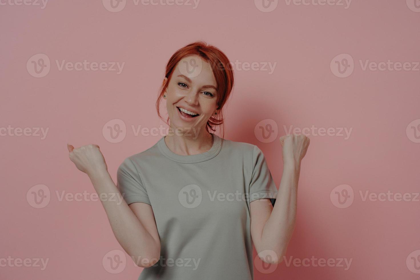 donna dai capelli rossi felicissima che celebra la vittoria, facendo il gesto del vincitore su sfondo rosa foto