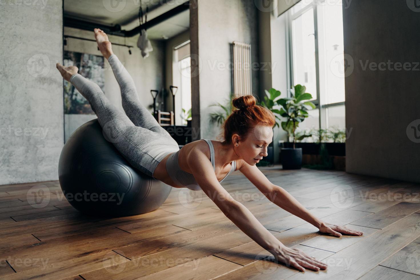 giovane donna sportiva zenzero che fa esercizi di stretching sulla palla da ginnastica di stabilità foto