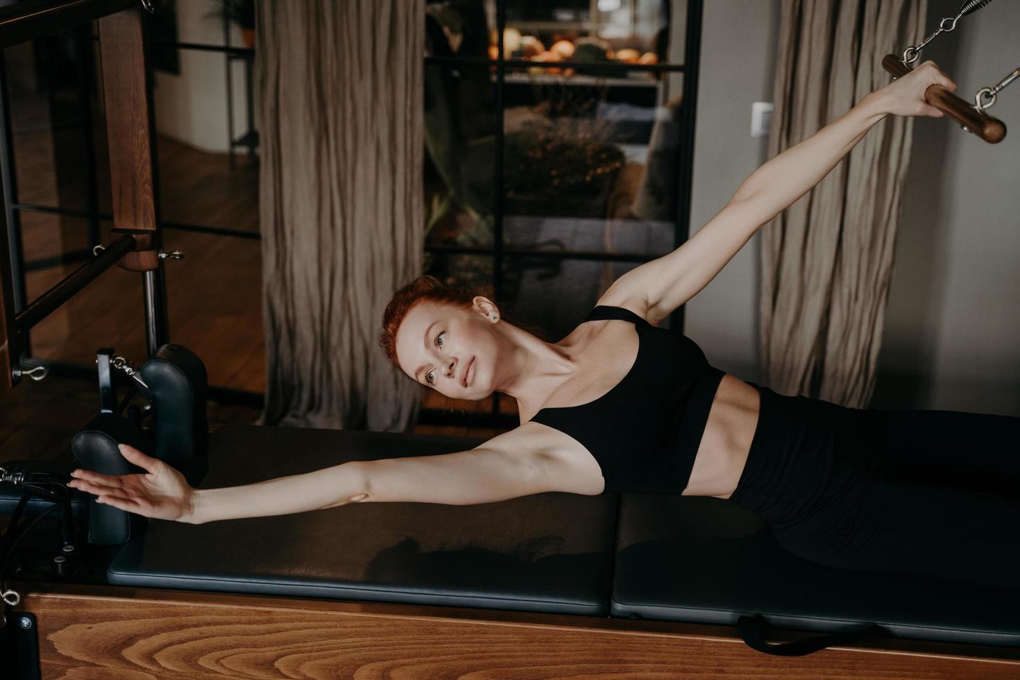 giovane istruttore di pilates femminile sdraiato nella posizione del braccio di allungamento su cadillac reformer foto
