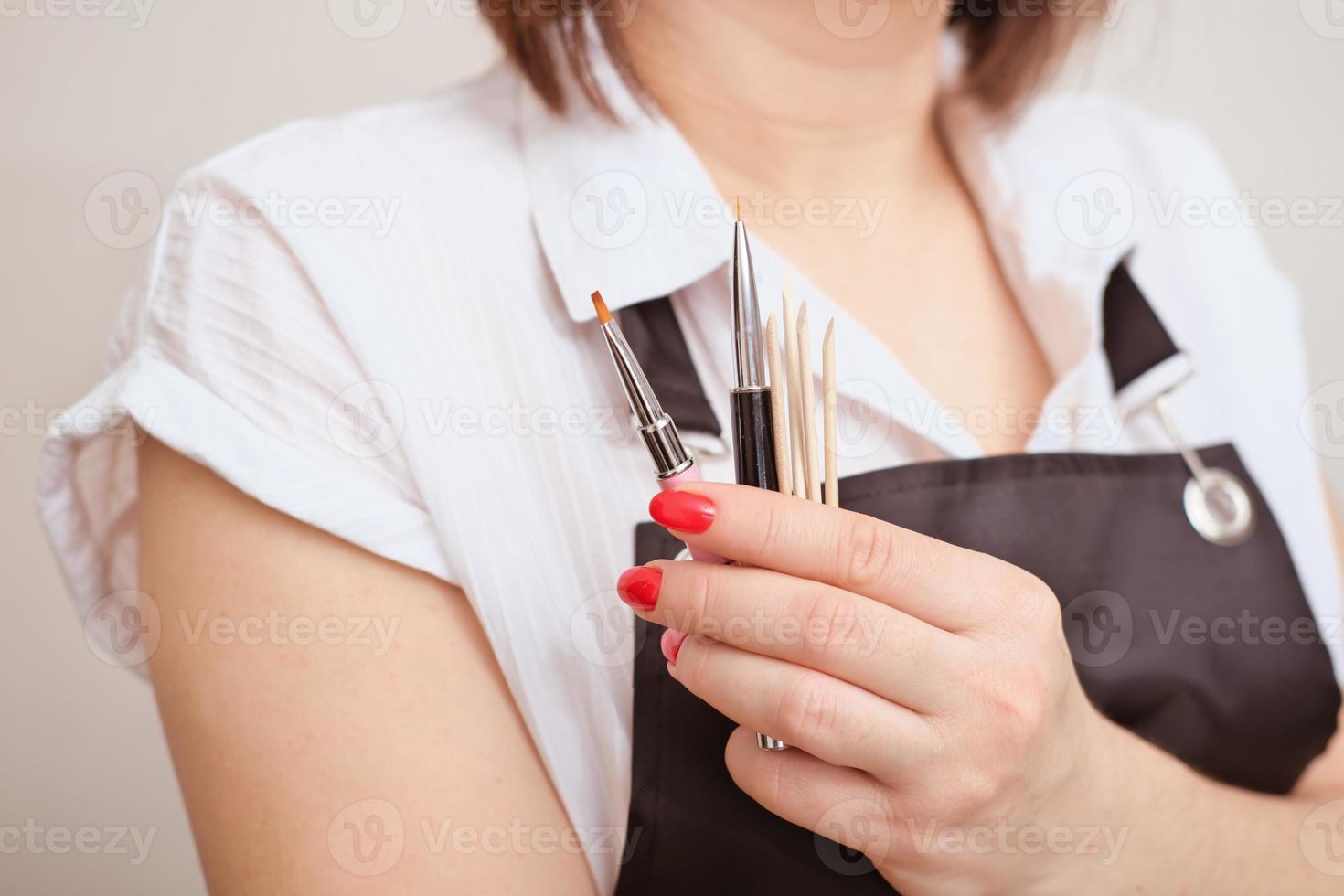 donna che indossa un grembiule con spazzole e bastoncini per manicure. accessori per la cura delle unghie e l'applicazione dello smalto. cura di bellezza delle mani in salone. foto