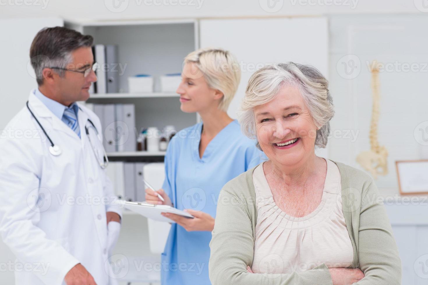 paziente sorridente mentre medico e infermiere discutendo in background foto