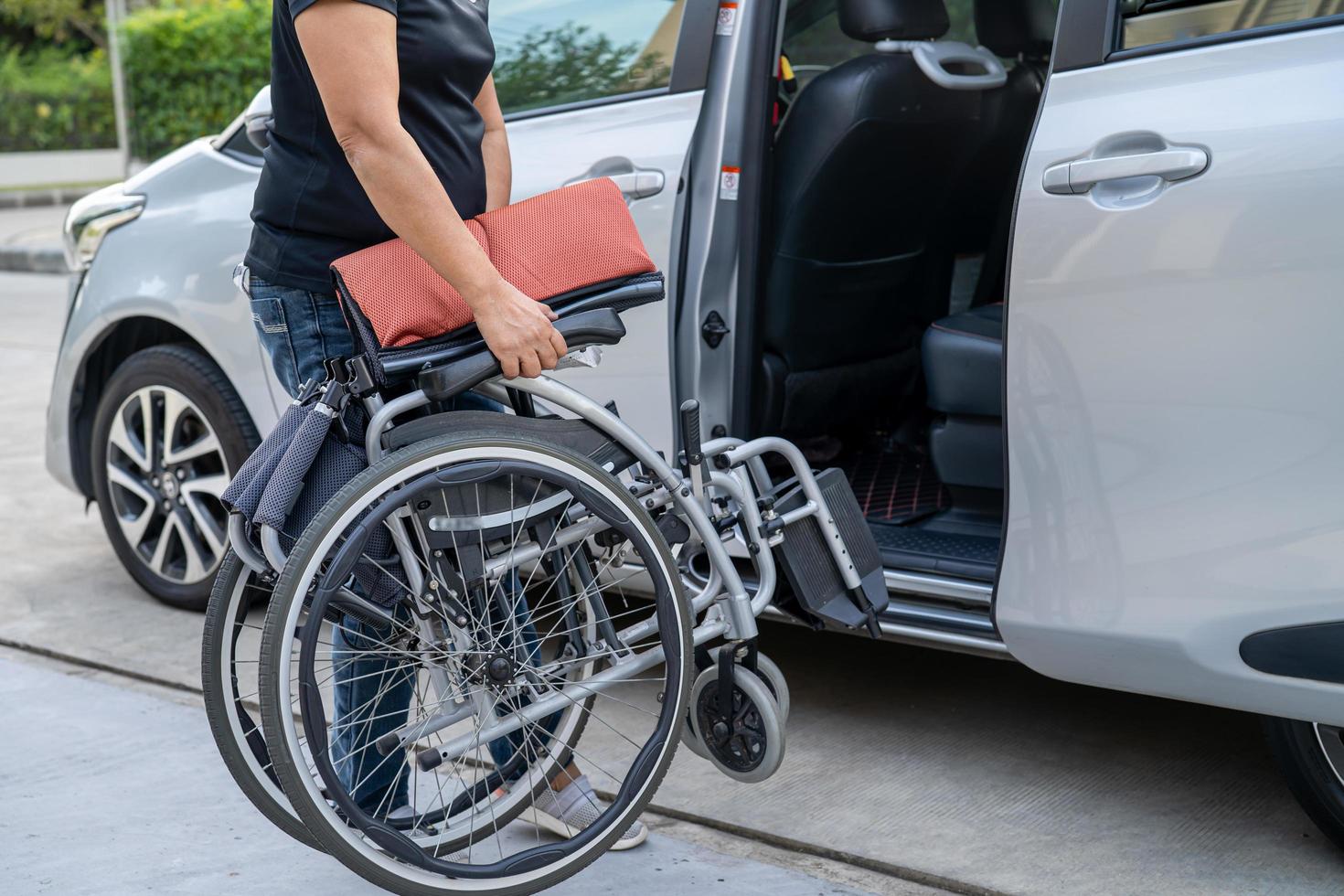 donna asiatica che piega e solleva la sedia a rotelle nella sua auto. concetto di accessibilità. foto